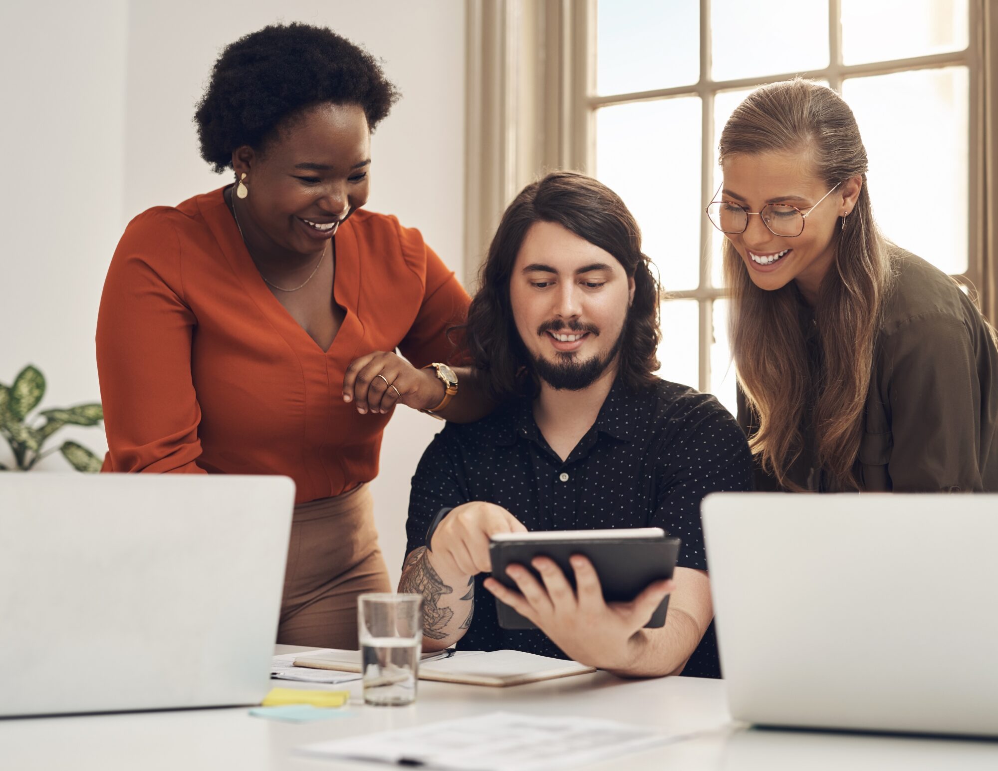 Three students smiling while looking at a tablet during a language lesson
